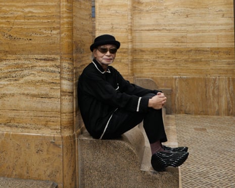 The Japanese musician Haruomi Hosono clad in black and sitting on a marble step