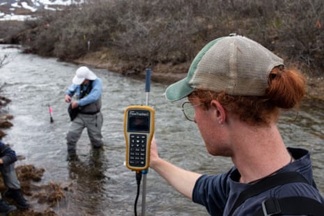 two men in hats holding scientific equipment standing in a river measuring something