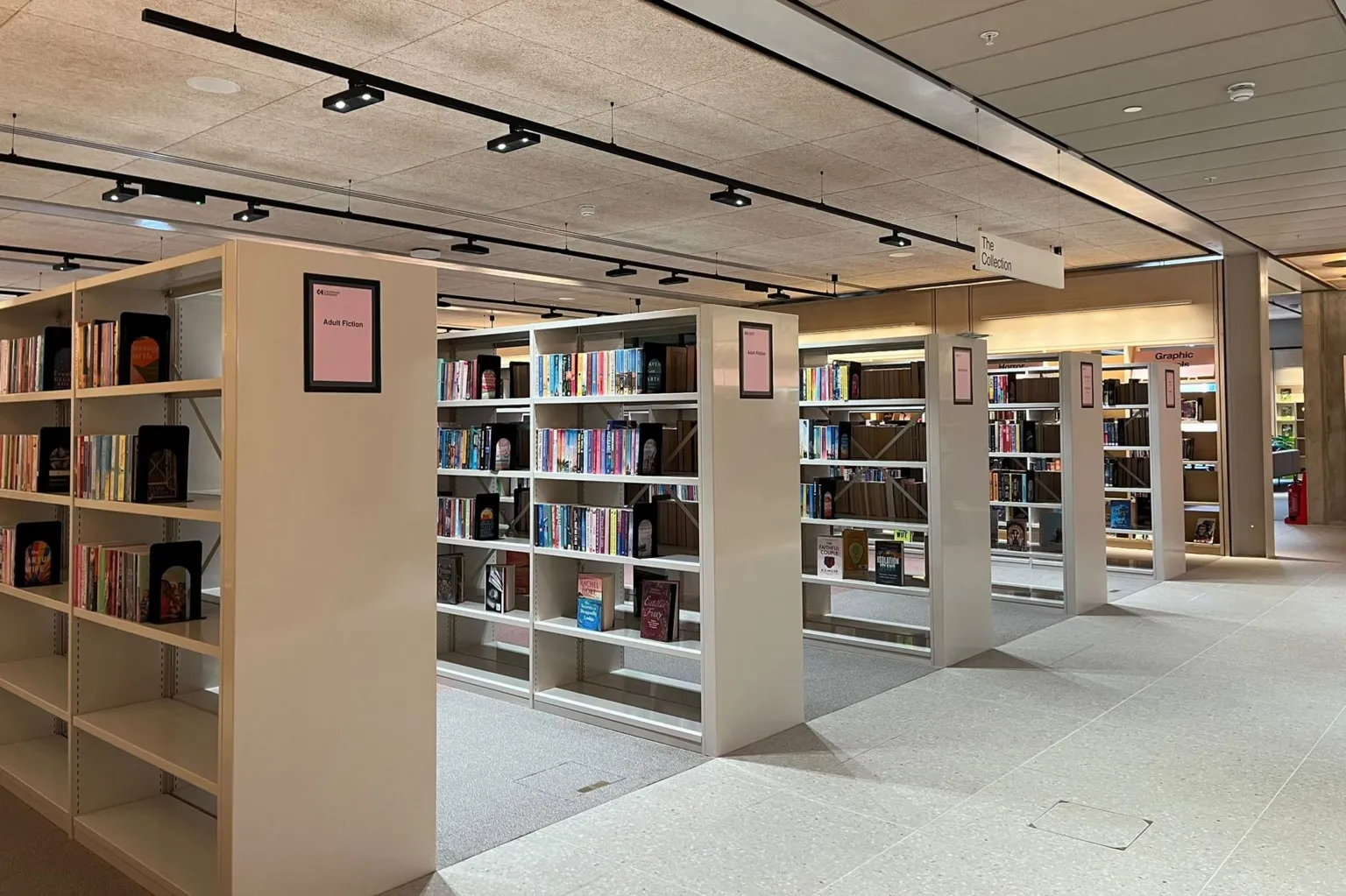 BBC / Kay Davidson There are rows of white bookshelves which are partially filled with books. The floor and the ceiling are also white, with rows of black spotlights overhead.